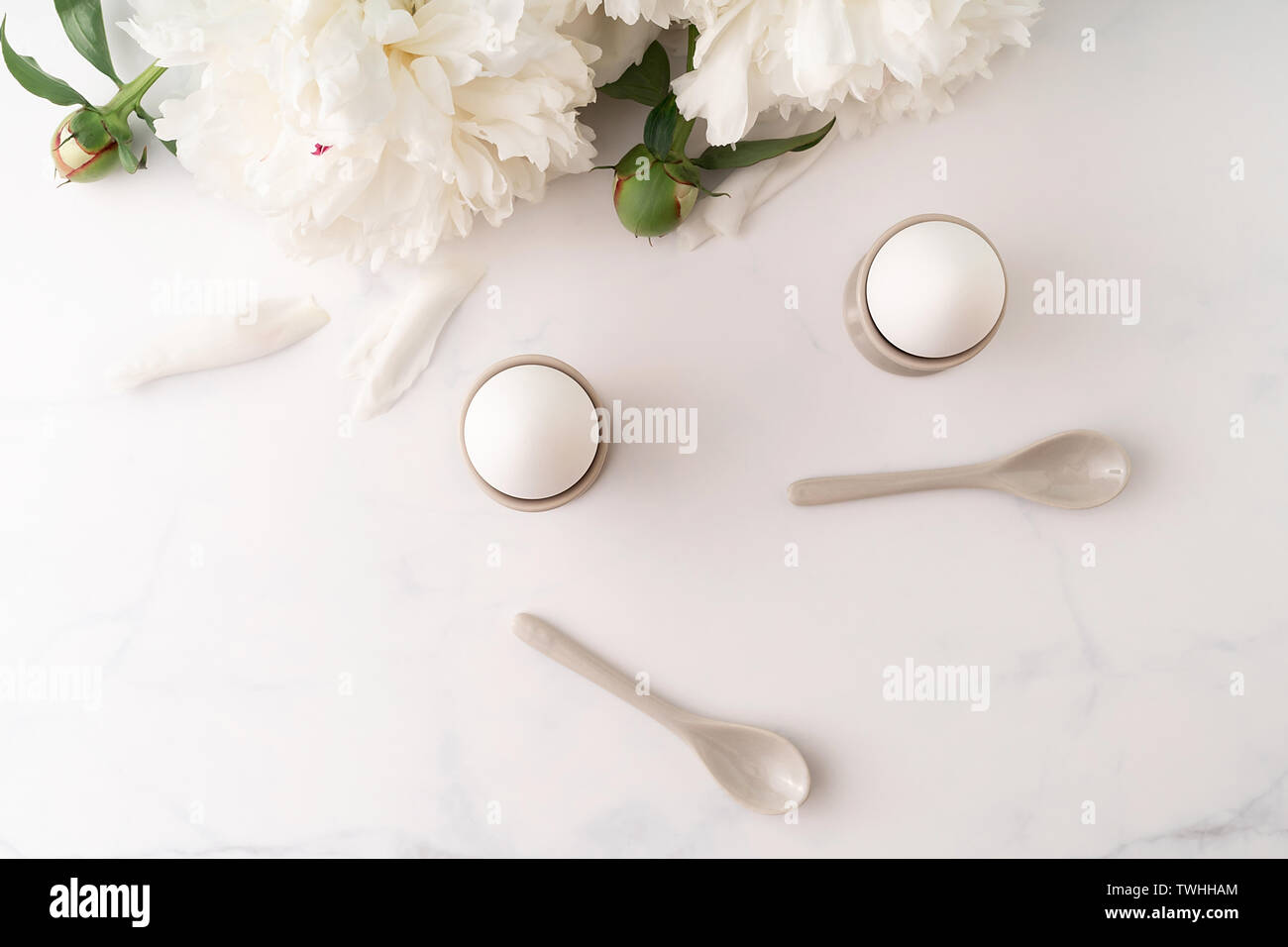 Oeufs durs oeufs en céramique tasses avec cuillères en céramique sur table de marbre haut décorée de beaux pivoine blanche. Le petit-déjeuner gratuit. Vue d'en haut. Copier l'espace. Banque D'Images