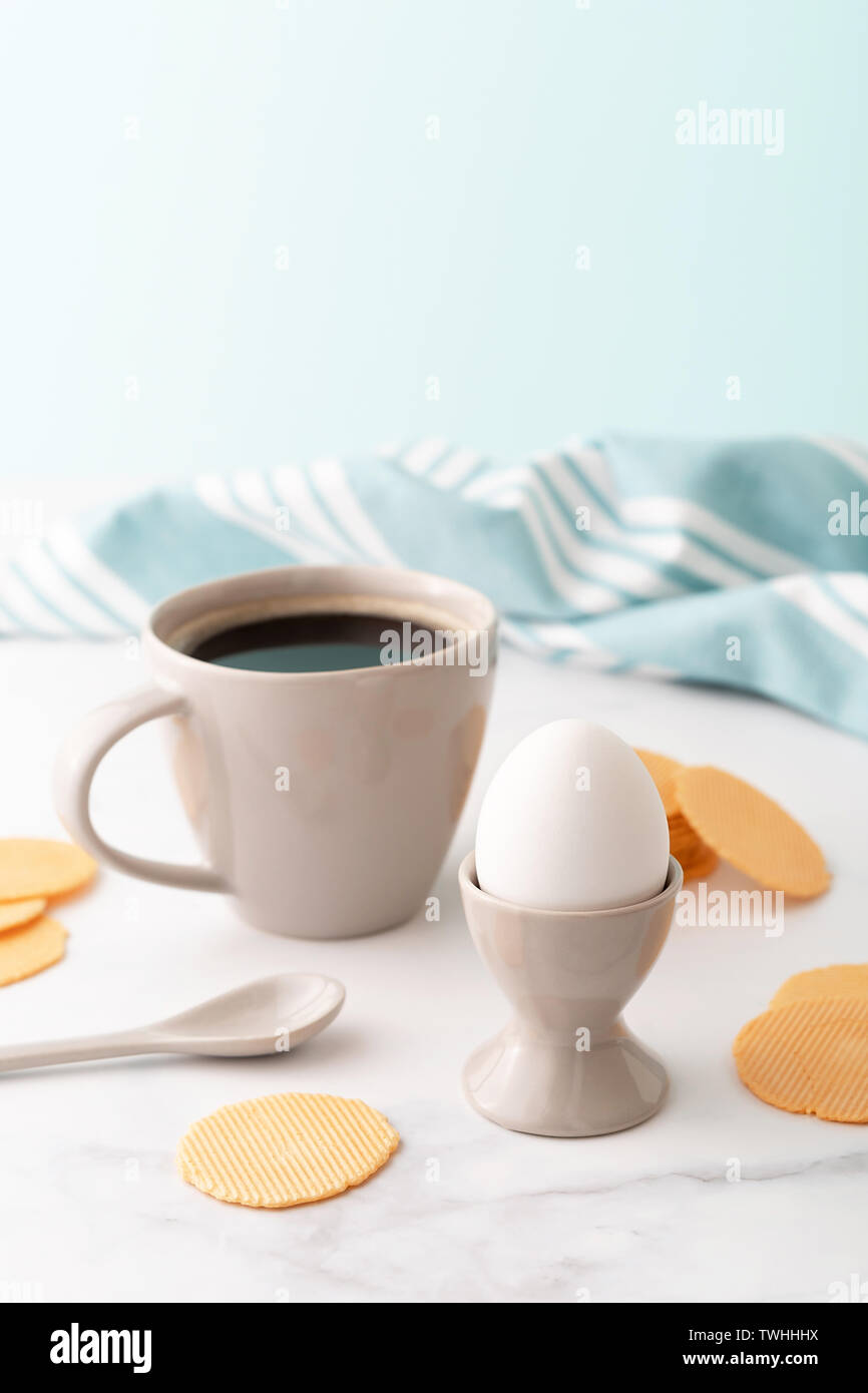 Oeuf dur en céramique egg cup, tasse de café et les croustilles de maïs mince et croustillante sur fond de belle pivoine blanche. Le petit-déjeuner gratuit. Copier l'espace. Banque D'Images