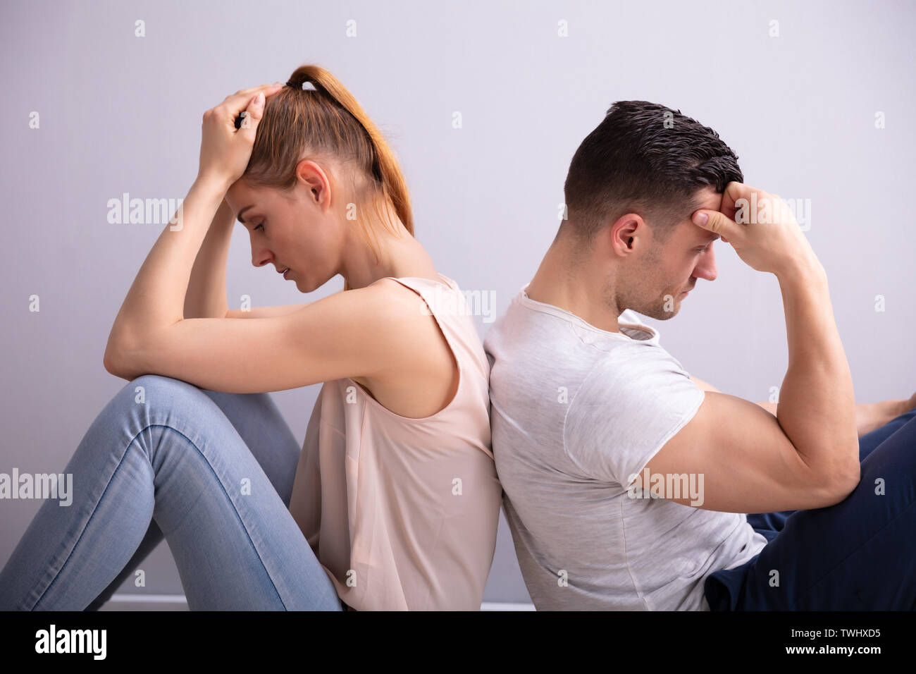 Triste jeune couple assis dos à dos sur le plancher à la maison Banque D'Images