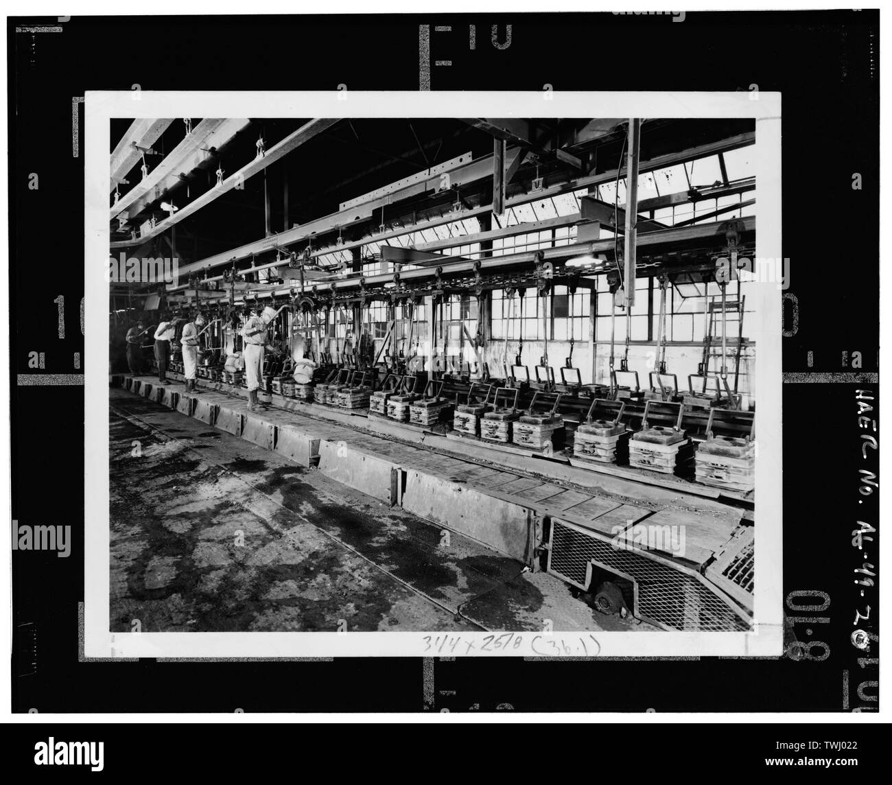 À l'instar du système installé dans la fonderie de fonte grise, Fonte malléable MOULES REMPLIS DE TRAVAILLEURS VOYAGEANT SUR UN CONVOYEUR DE LOUCHES ACCROCHÉES À RAILS PENDANT QUE ILS ÉTAIENT DEBOUT SUR UNE PLATE-FORME SE DÉPLAÇANT À la même vitesse que le convoyeur, CA. 1950 - les tuyaux et raccords Stockham Company, 4000 10e Avenue Nord, Comté de Jefferson, Birmingham, AL Banque D'Images