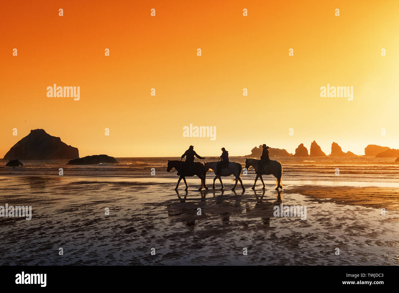 3 adultes de l'équitation au coucher du soleil sur la plage de Bandon en Oregon. Banque D'Images