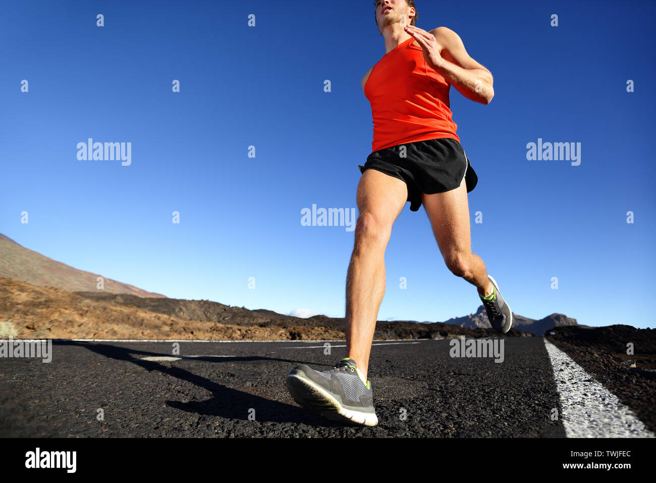 Sprint running man - male runner jogging à l'extérieur de la formation sur route de montagne dans un paysage extraordinaire de la nature. Close up of fit beau jogger marathon pour l'extérieur en été. Banque D'Images