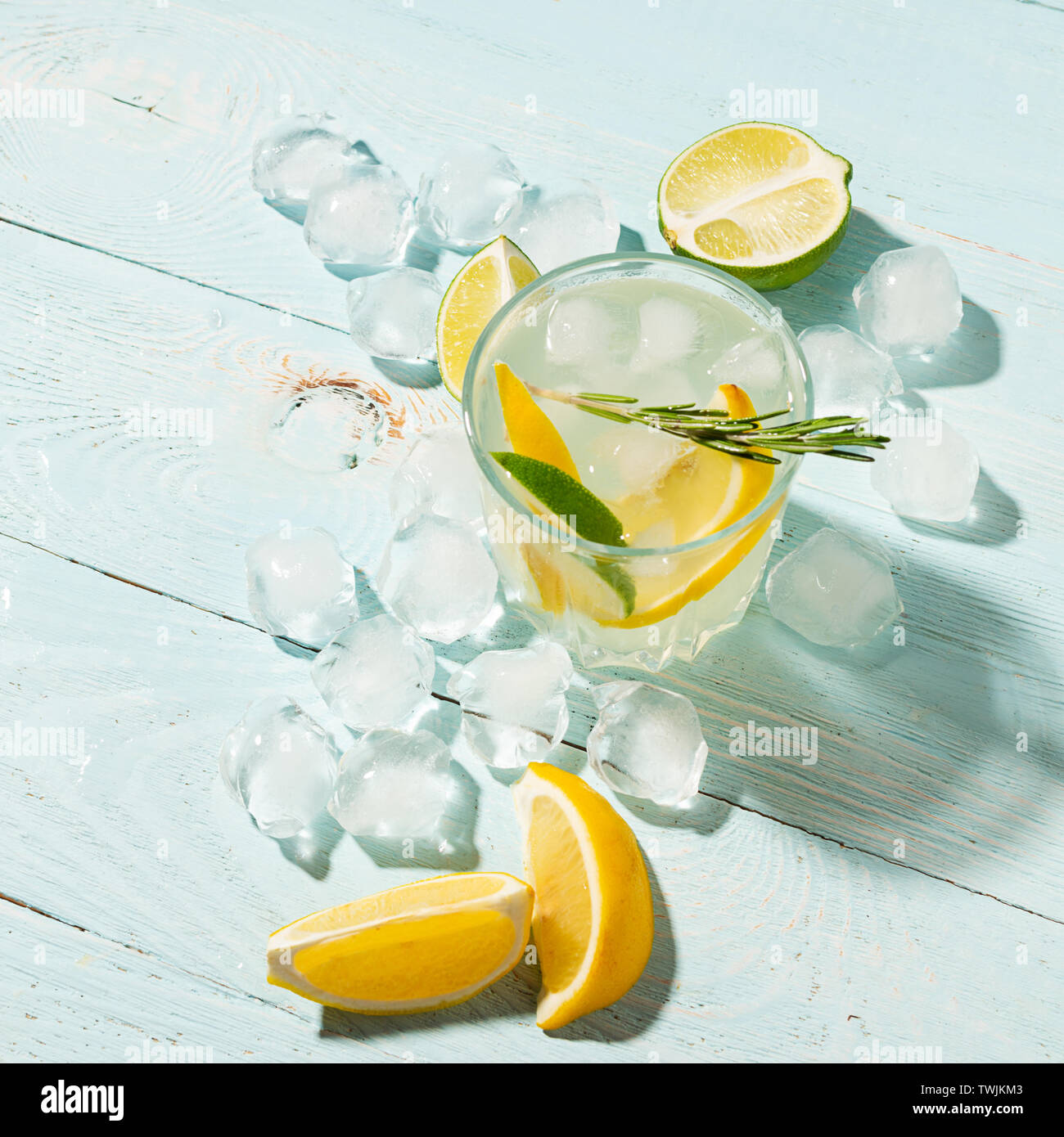 Un verre de citron et de lime dans un élégant verre sur un fond bleu avec un soleil brillant. Cocktail d'été ou mojito. Banque D'Images