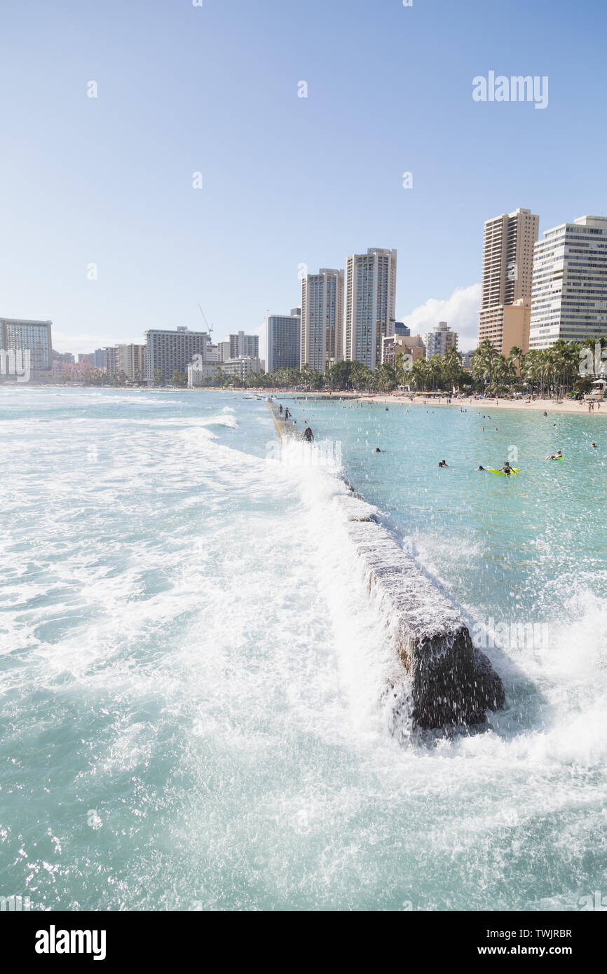 Les vagues frapper la digue tandis que les touristes et les habitants de marche sur elle à Kuhio Beach Park dans la plage de Waikiki, Oahu, Hawaii. Banque D'Images