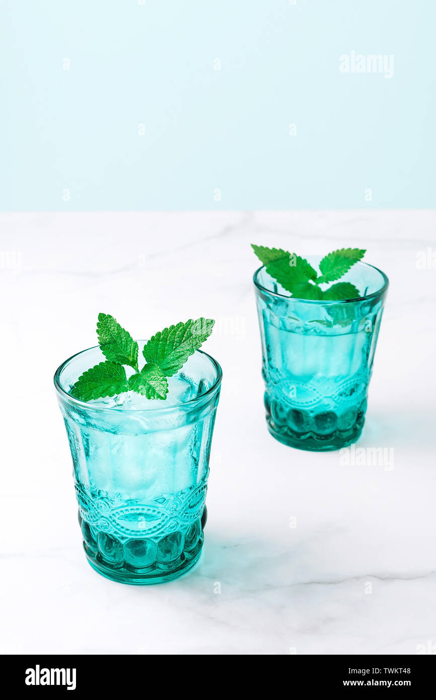 Deux beaux verres turquoise vintage avec boisson froide et des cubes de glace, décoré de feuilles de menthe verte fraîche sur la table de marbre blanc. Close-up. Banque D'Images