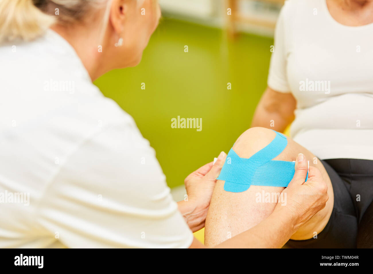 Physiothérapeute attache un ruban kinesio au genou d'un patient pour le soulagement de douleur Banque D'Images