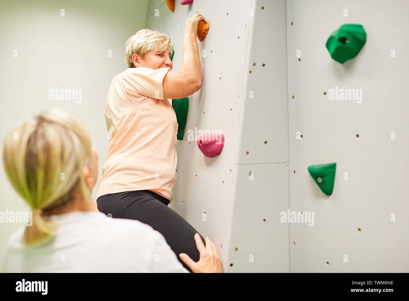 Senior woman climbing dans une salle d'escalade pour la coordination et la forme physique avec soin Banque D'Images
