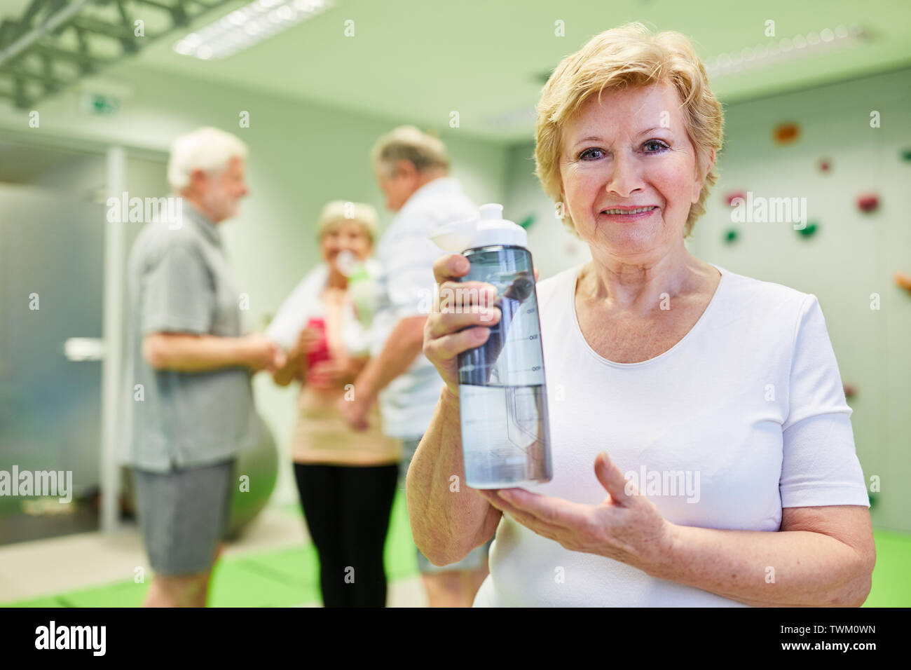 Femme senior vital avec une bouteille d'eau au cours d'une pause dans le parcours dans la salle d'escalade Banque D'Images