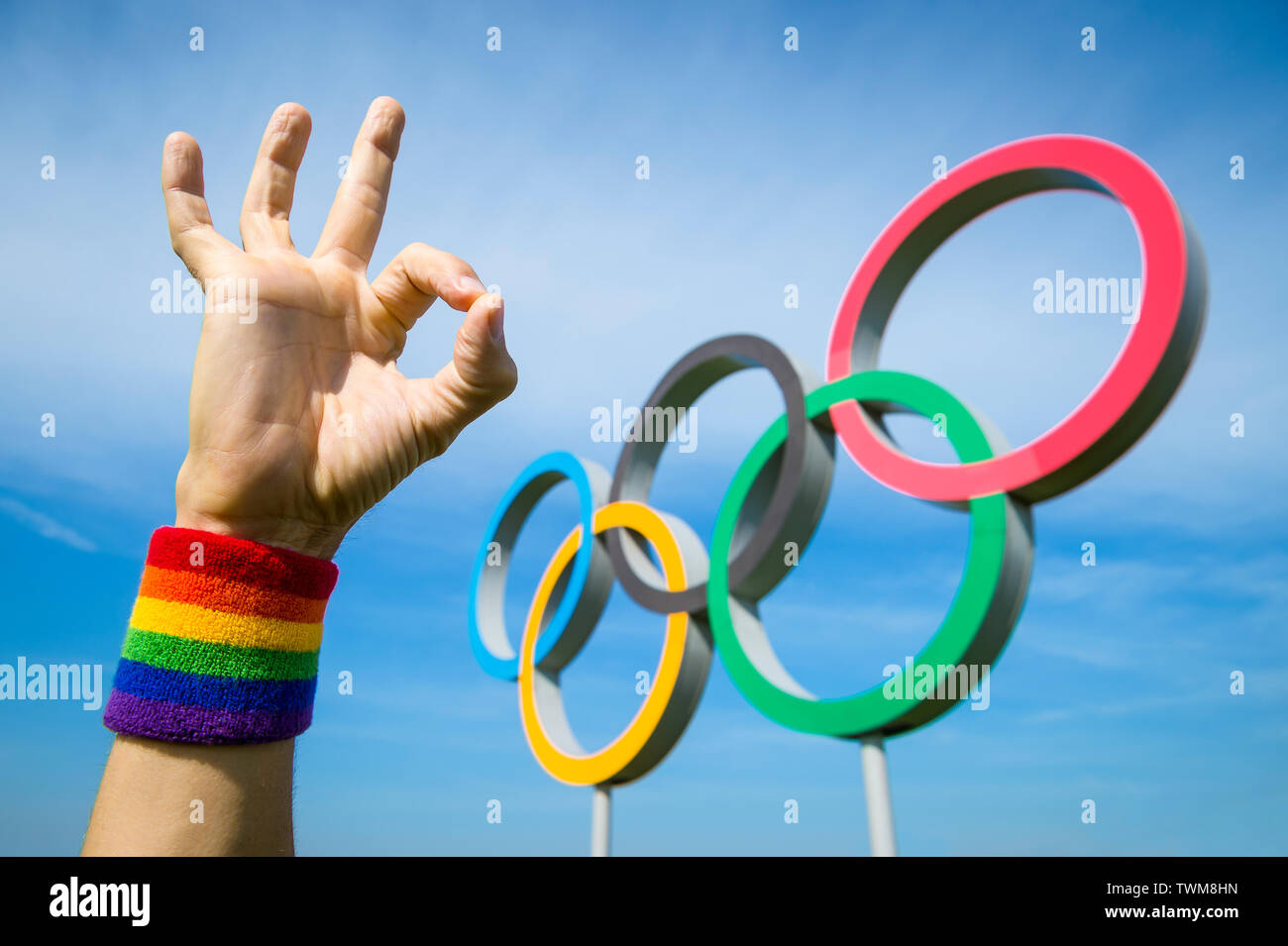 Londres - 4 mai 2019 : une main portant des gay pride rainbow bracelet de couleur fait un geste OK en face d'anneaux olympiques sous ciel bleu. Banque D'Images