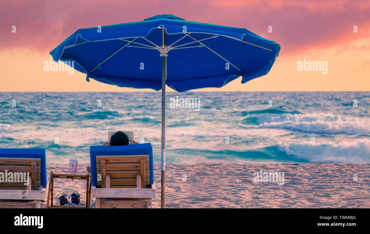 L'homme lit livre sur Florida Beach avec un lever du soleil orange rose Banque D'Images