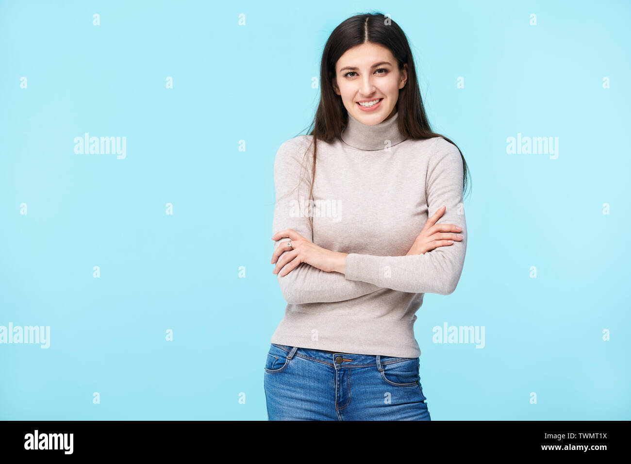 Studio portrait d'une jolie femme de race blanche, les bras croisés, smiling at camera, isolé sur fond bleu Banque D'Images