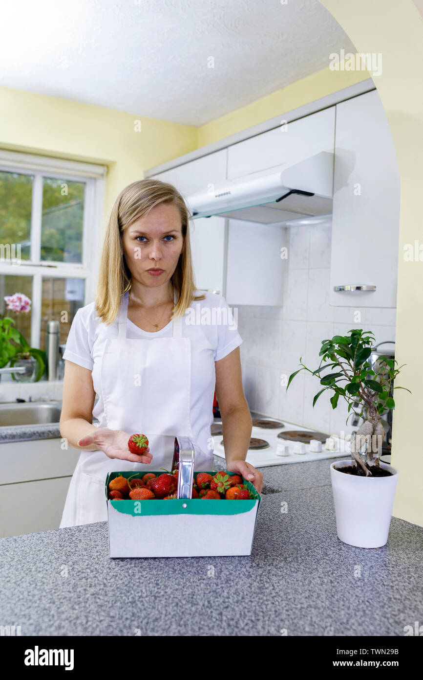 Une jeune femme qui cuisine à la maison. Une fille tient un panier de fraises biologiques dans la cuisine. Des fraises fraîches sont en cours de préparation Banque D'Images