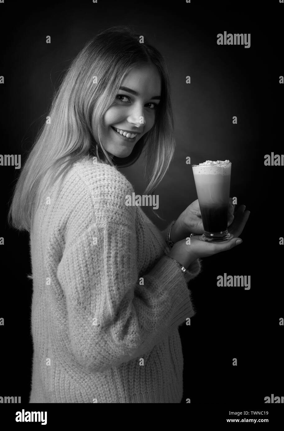 Beautiful smiling girl dans un chandail tenant un cocktail du café avec de la crème. Noir et blanc. Banque D'Images