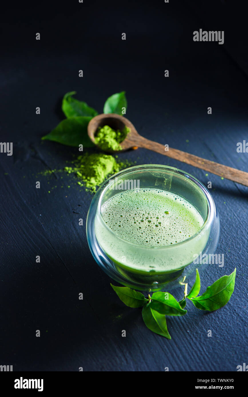 Thé Matcha avec de la mousse dans une double paroi en verre avec une cuillère en bois avec matcha en poudre sur un fond sombre avec copie espace Banque D'Images