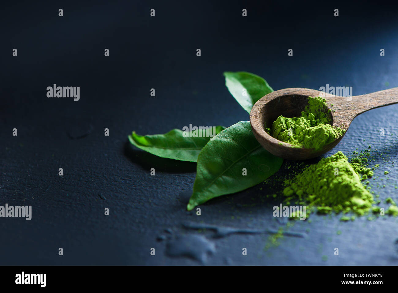 Thé Matcha en poudre dans les feuilles de thé avec une cuillère de bois sur un fond sombre avec copie espace Banque D'Images