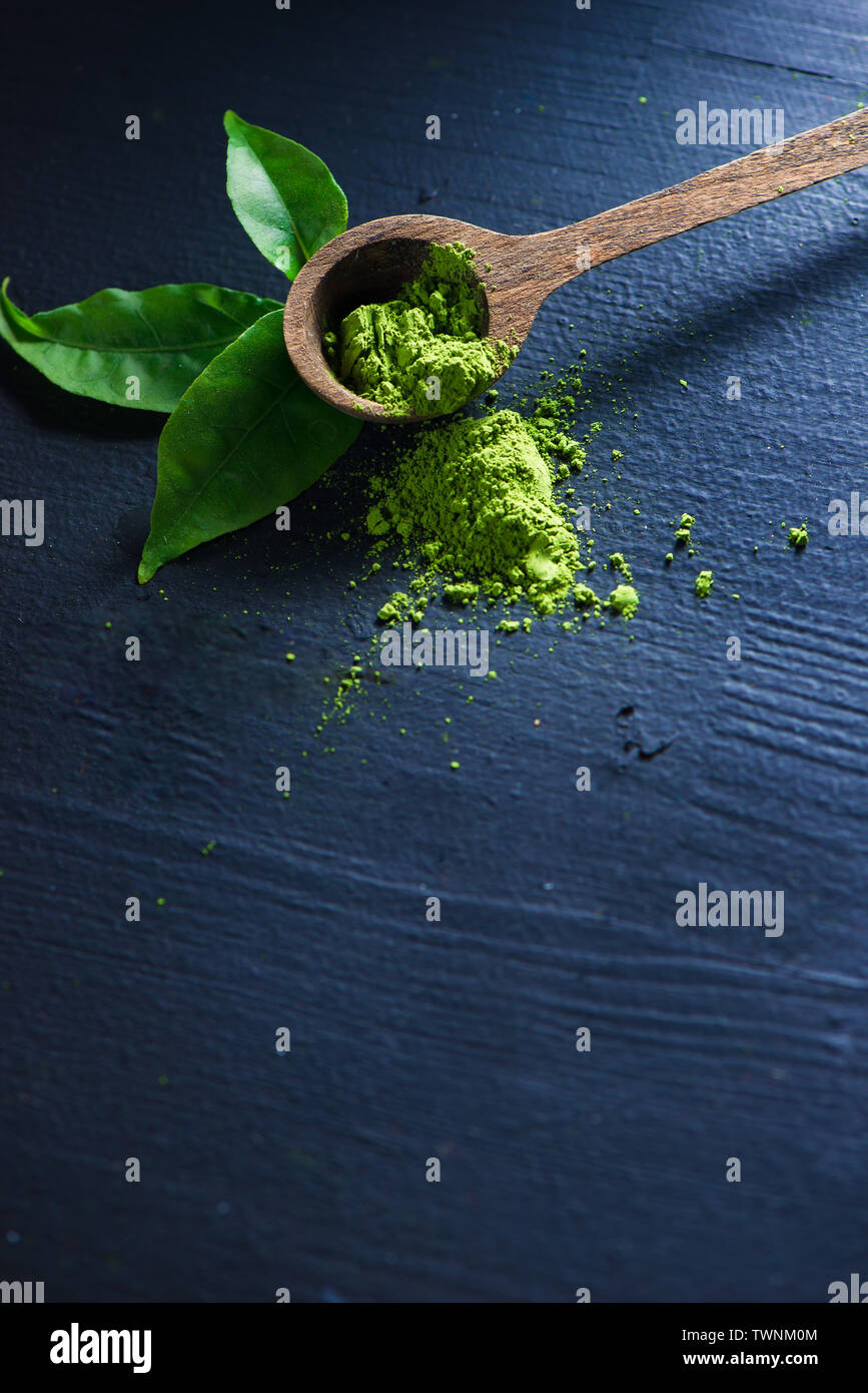 Thé Matcha en poudre dans les feuilles de thé avec une cuillère de bois sur un fond sombre avec copie espace Banque D'Images