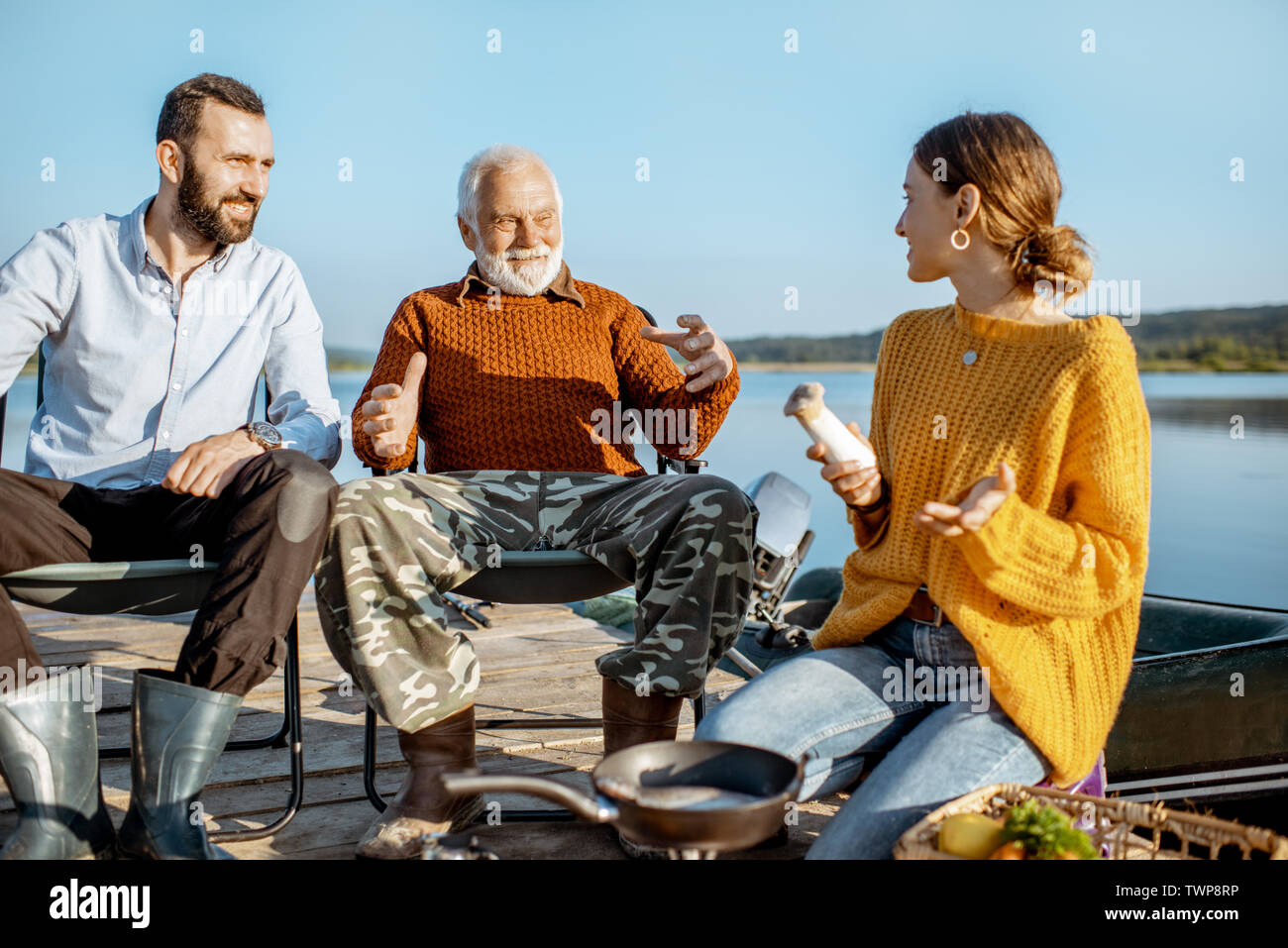 L'homme et la femme ayant la conversation chaleureuse avec des grand-père pendant le pique-nique près du lac, dans le matin Banque D'Images