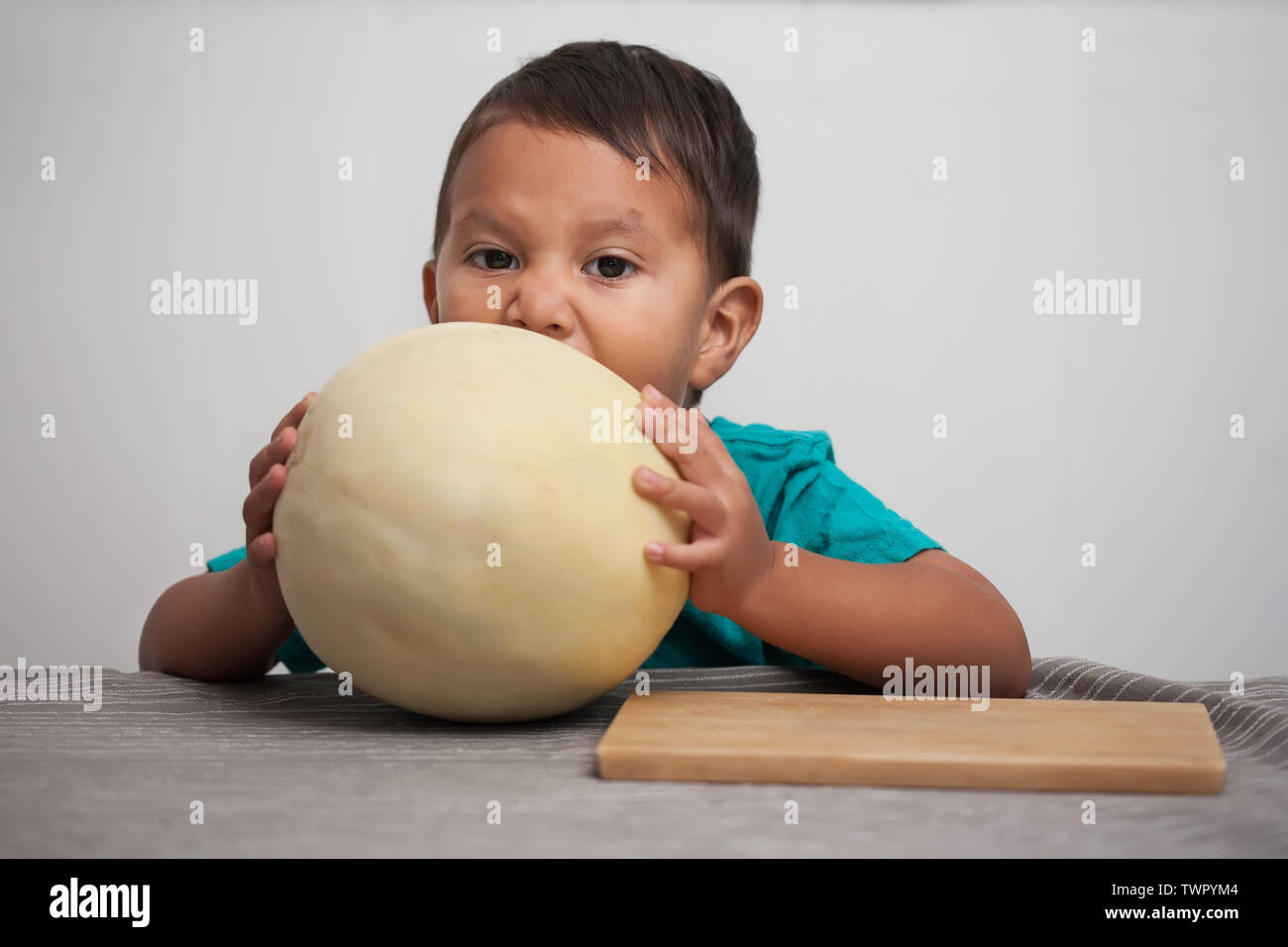 Un enfant impatient d'essayer dur pour prendre une bouchée d'un honeymelon il tient dans sa main avant d'être servi. Banque D'Images