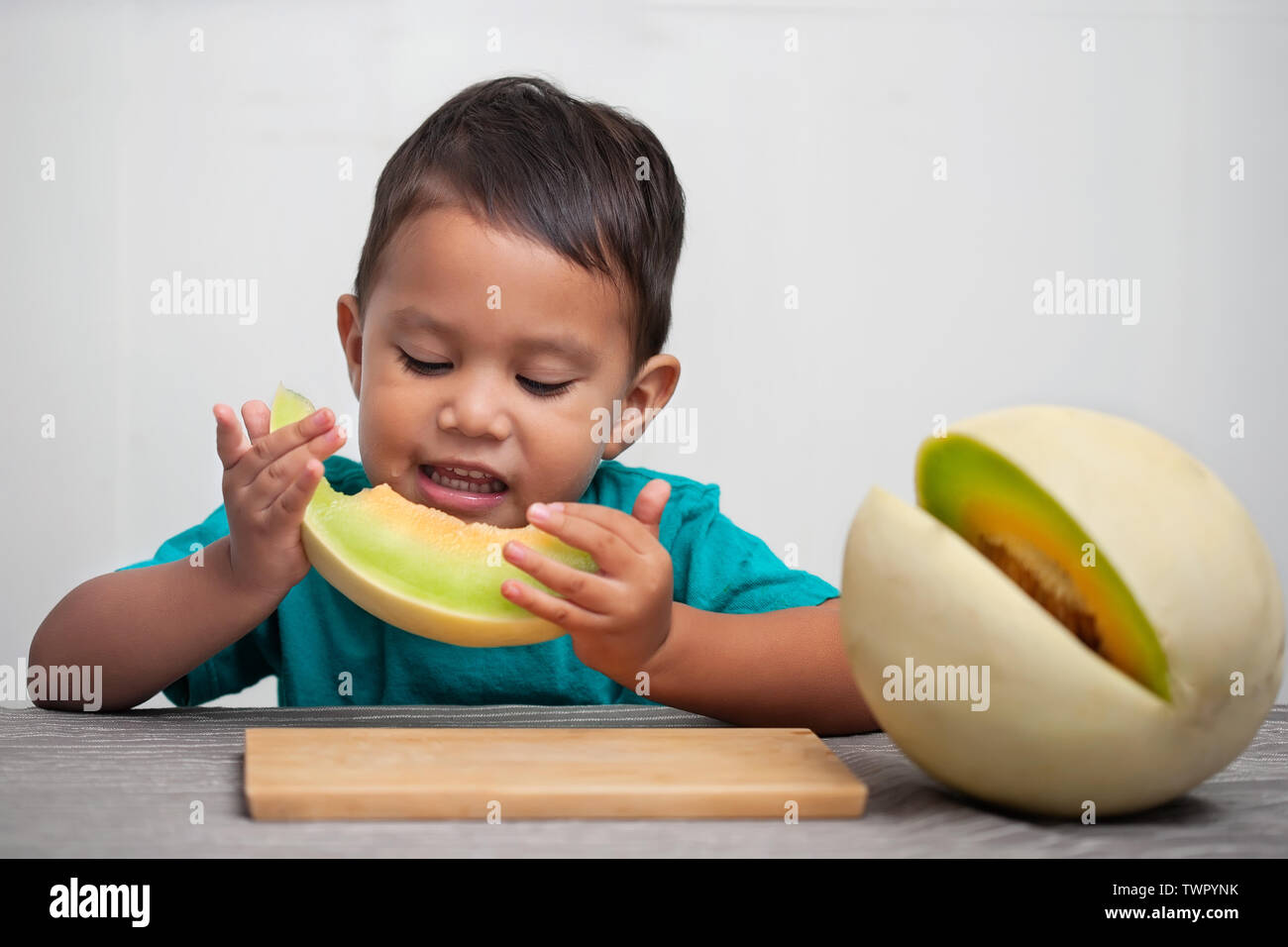 Un petit garçon tenant une tranche de melon frais fruit à sa bouche qu'il a pris une bouchée, et d'apprécier le goût sucré et juteux. Banque D'Images