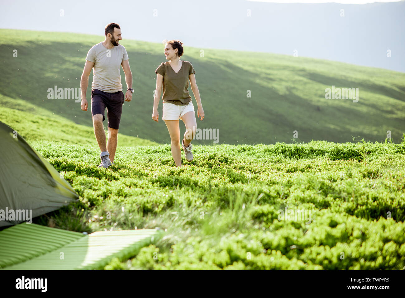 Jeune couple en train de marcher sur le pré vert à proximité du camping tout en voyageant dans les montagnes Banque D'Images