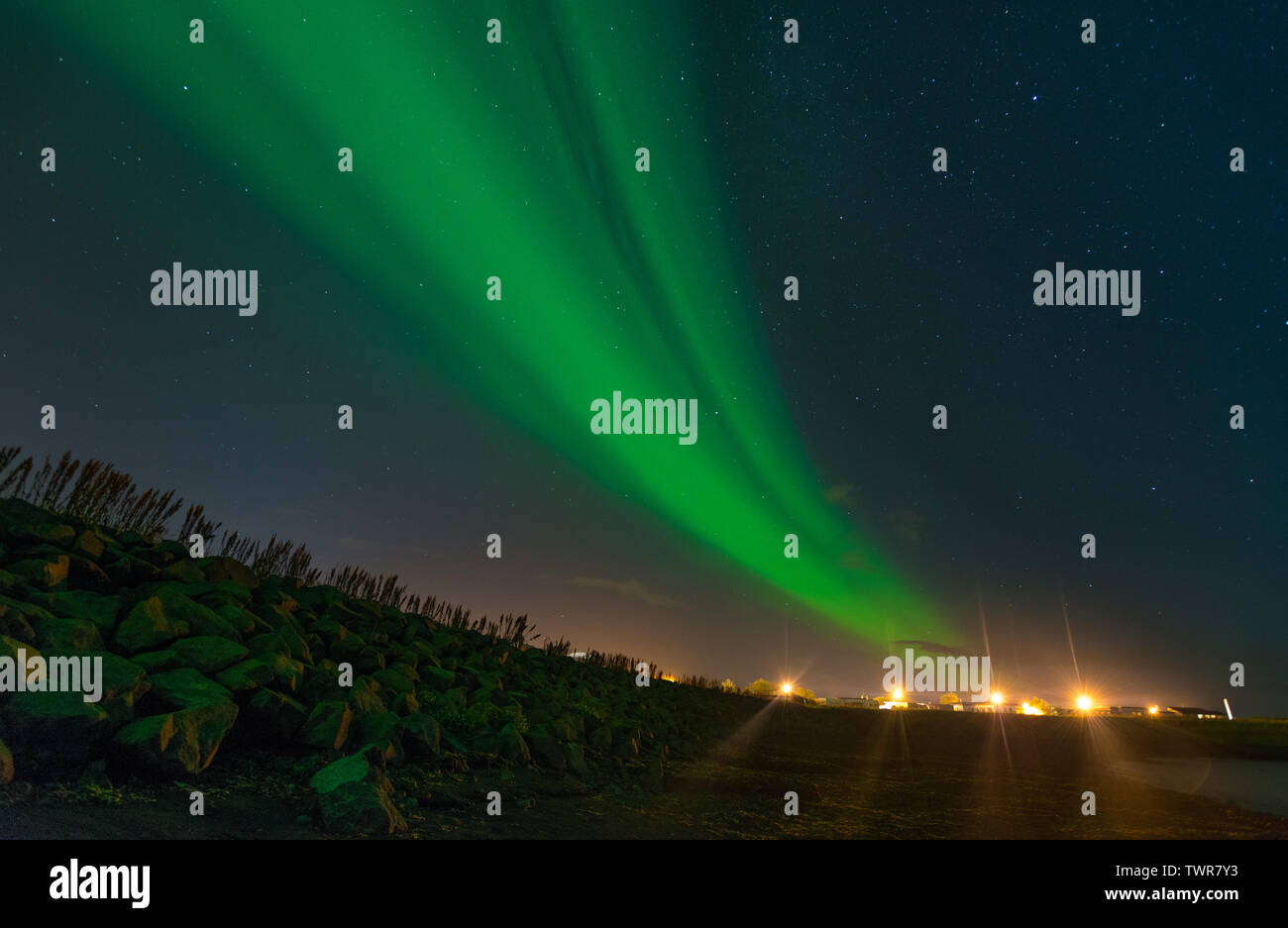 Un vert d'aurores boréales, entrelardées northern lights découlant des lumières de la ville. L'Arctique bleu ciel avec Aurora et les lumières de la ville. Banque D'Images