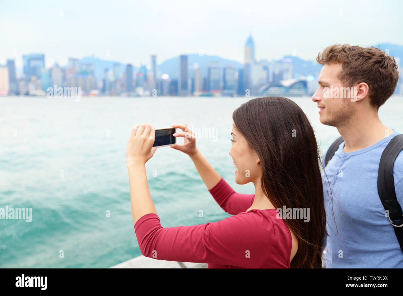 Tourist couple taking photo photos enjoying view et le tourisme sur la promenade de Tsim Sha Tsui et de l'Avenue des Stars à Victoria Harbour, Kowloon, Hong Kong. Concept de l'industrie du tourisme. Banque D'Images