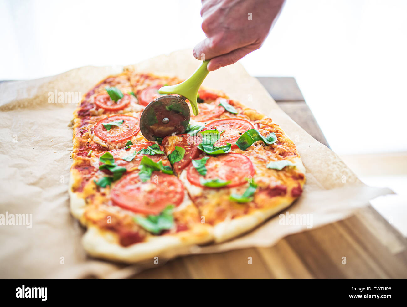 High angle view of hand cutting pizza Margherita maison délicieux avec des tomates et basilic à l'aide d'un coupe-pizza Banque D'Images
