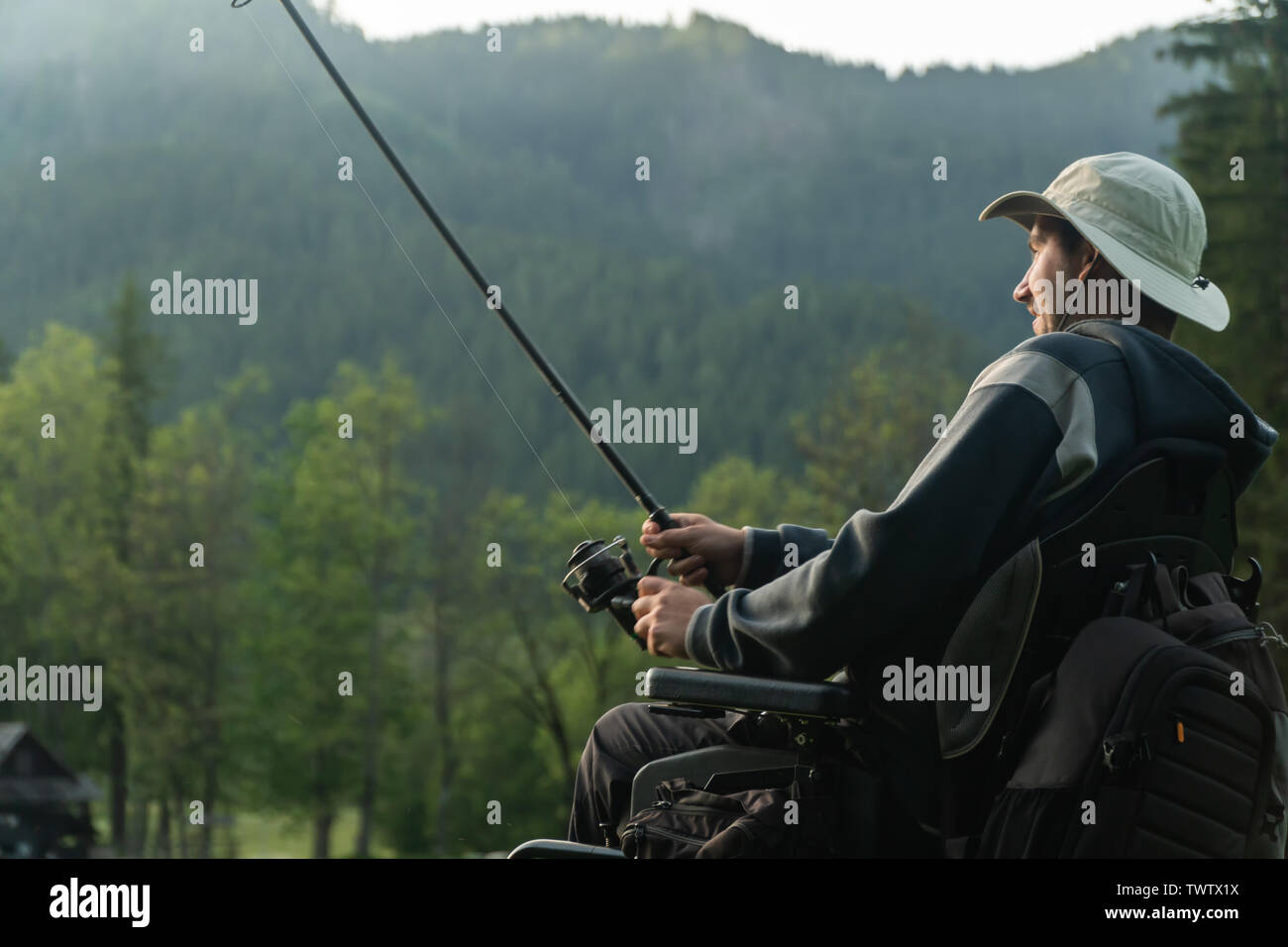 Jeune homme en fauteuil roulant la pêche dans le magnifique lac dans le coucher du soleil, l'aube Banque D'Images