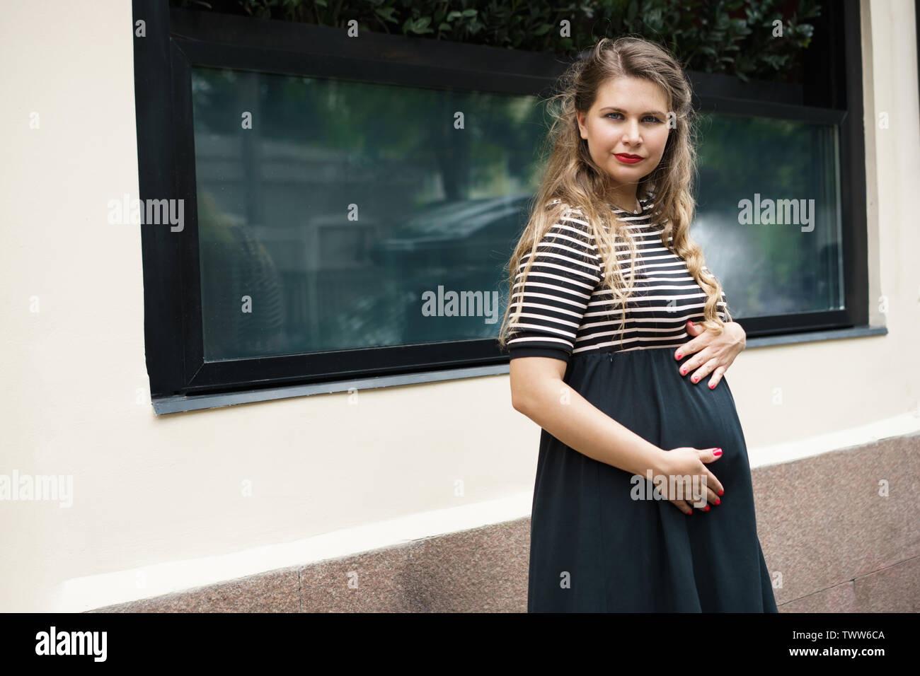 Une femme enceinte dans un noir et blanc robe rayée avec de longs cheveux blonds Banque D'Images