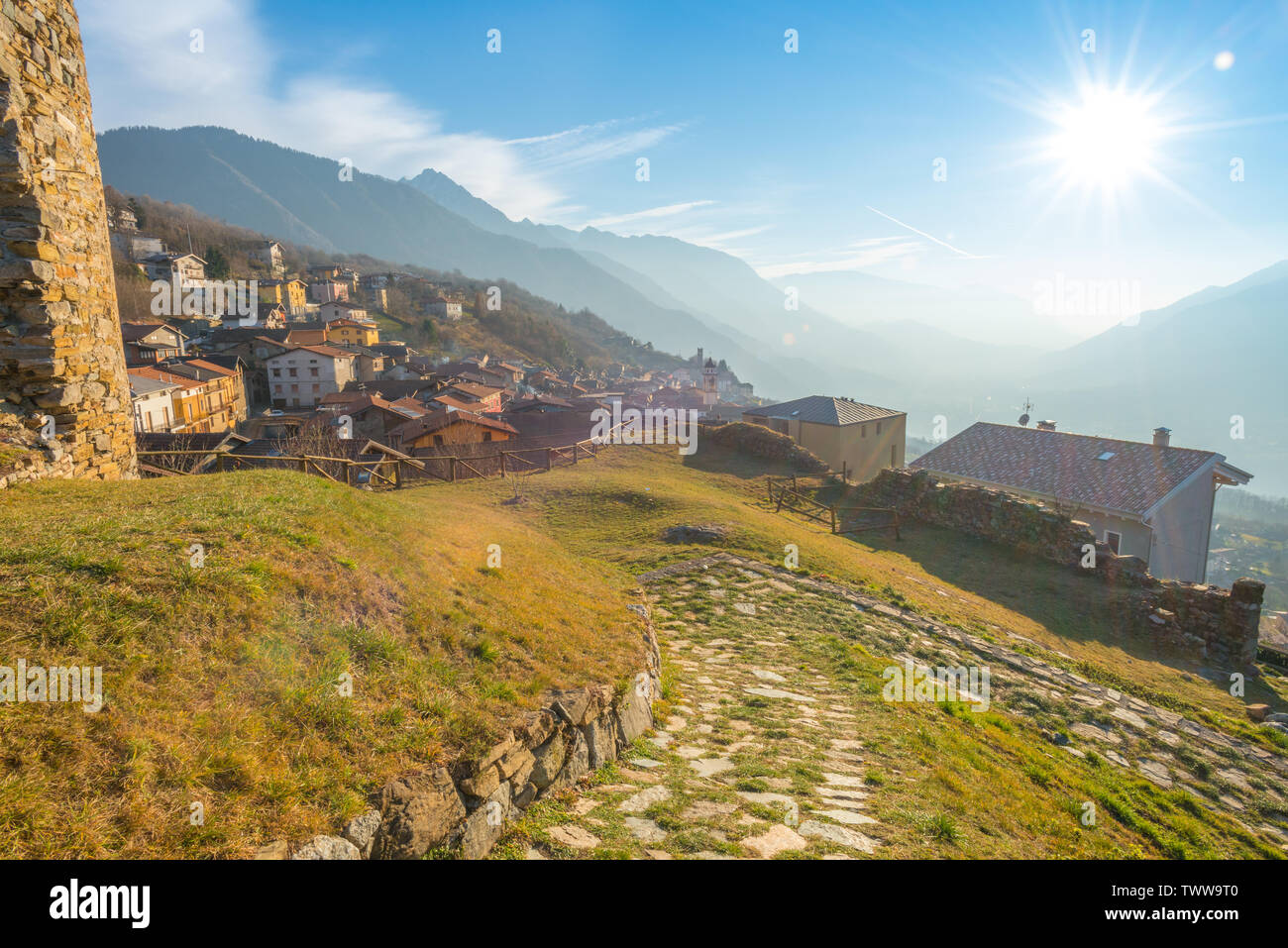 Rayons de soleil sur la ville de Cimbergo, soleil qui brille sur les maisons et les montagnes de la vallée. Chemin de pierre menant au belvédère au-dessus de la ville. Banque D'Images