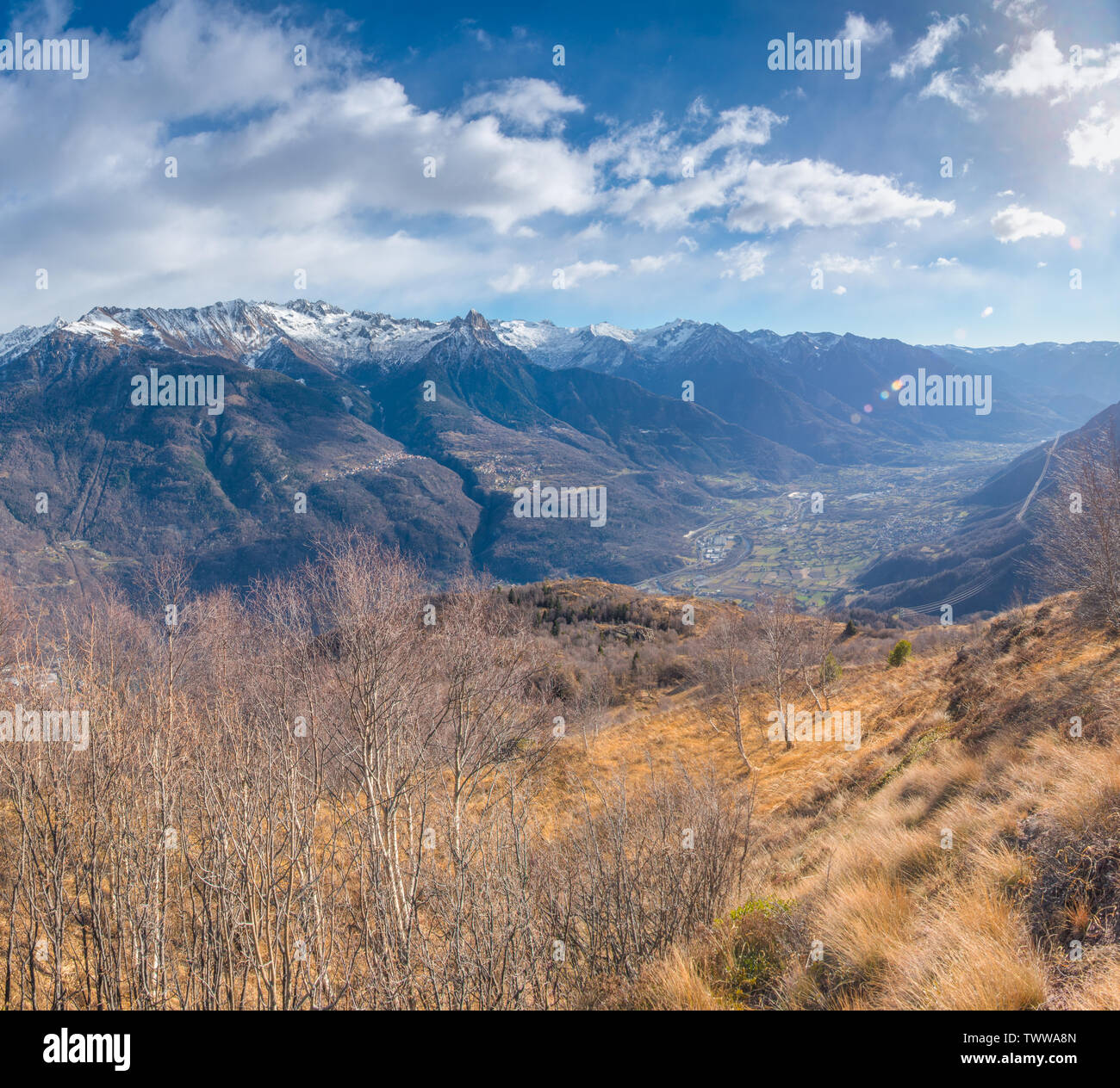 La lumière du soleil sur la végétation sèche de l'hiver dans les montagnes du Val Camonica, Alpes italiennes. Montagnes aux sommets enneigés au fond de vallée, les rayons du soleil. Banque D'Images