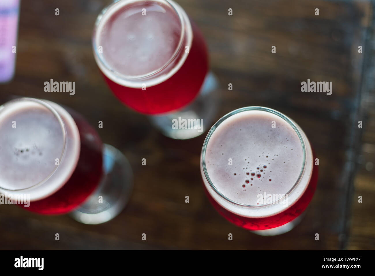 Trois verres de vin rouge sur une table en bois. Verres de bière cerise sont sur la table. Un groupe de personnes les boissons au bar. Il n'y a personne dans le cadre. Banque D'Images