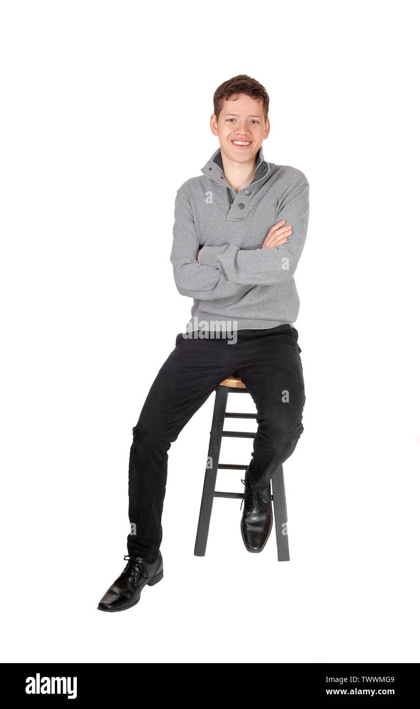 Un jeune garçon de l'adolescence, assis dans un chandail gris, les bras croisés sur une chaise, souriant pour isolé sur fond blanc Banque D'Images