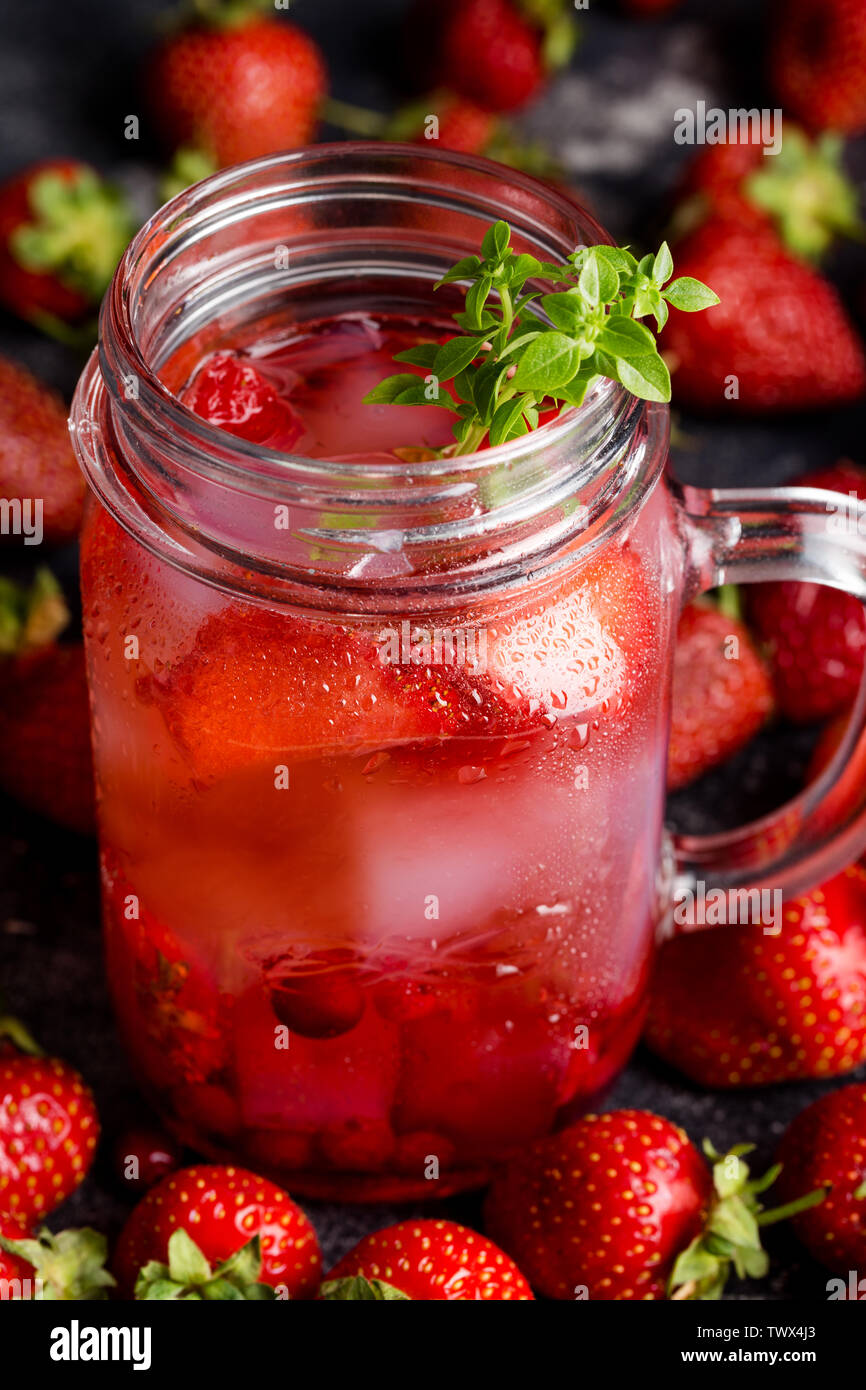 Close up limonade aux fraises avec de la glace en pot aux fruits rouges et basilic autour sur fond sombre. Banque D'Images