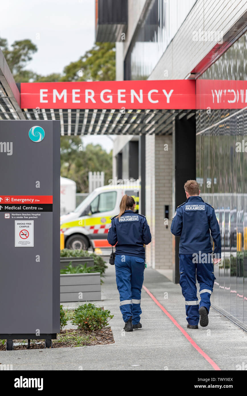 Deux jeunes hommes blancs et des femmes officiers d'ambulanciers paramédicaux à pied vers une ambulance et panneau d'urgence à Sydney de neuf plages du Nord Hospital Banque D'Images
