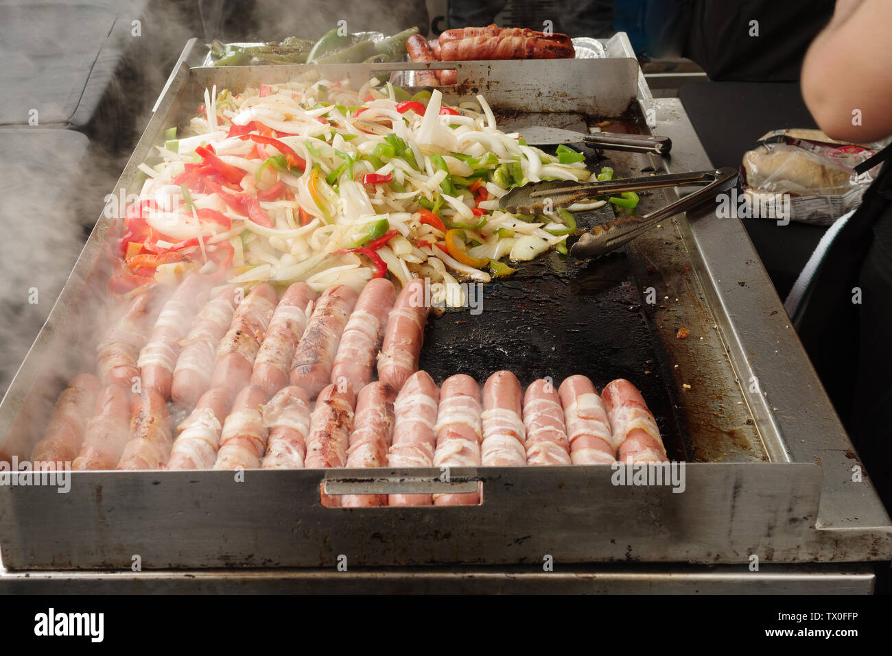 Hot-dogs, oignons, poivrons verts et poivrons rouges cuisant sur grill chaud. Banque D'Images