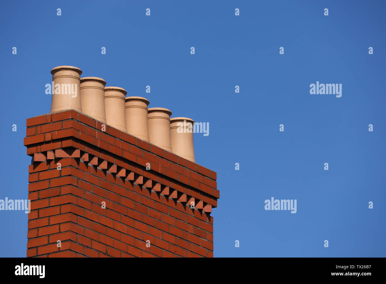 L'argile en terre cuite rouge victorien pots de cheminée monté en haut d'une cheminée en brique d'argile rouge illustré contre un ciel bleu. Prises à Cardiff, Pays de Galles, Royaume-Uni Banque D'Images