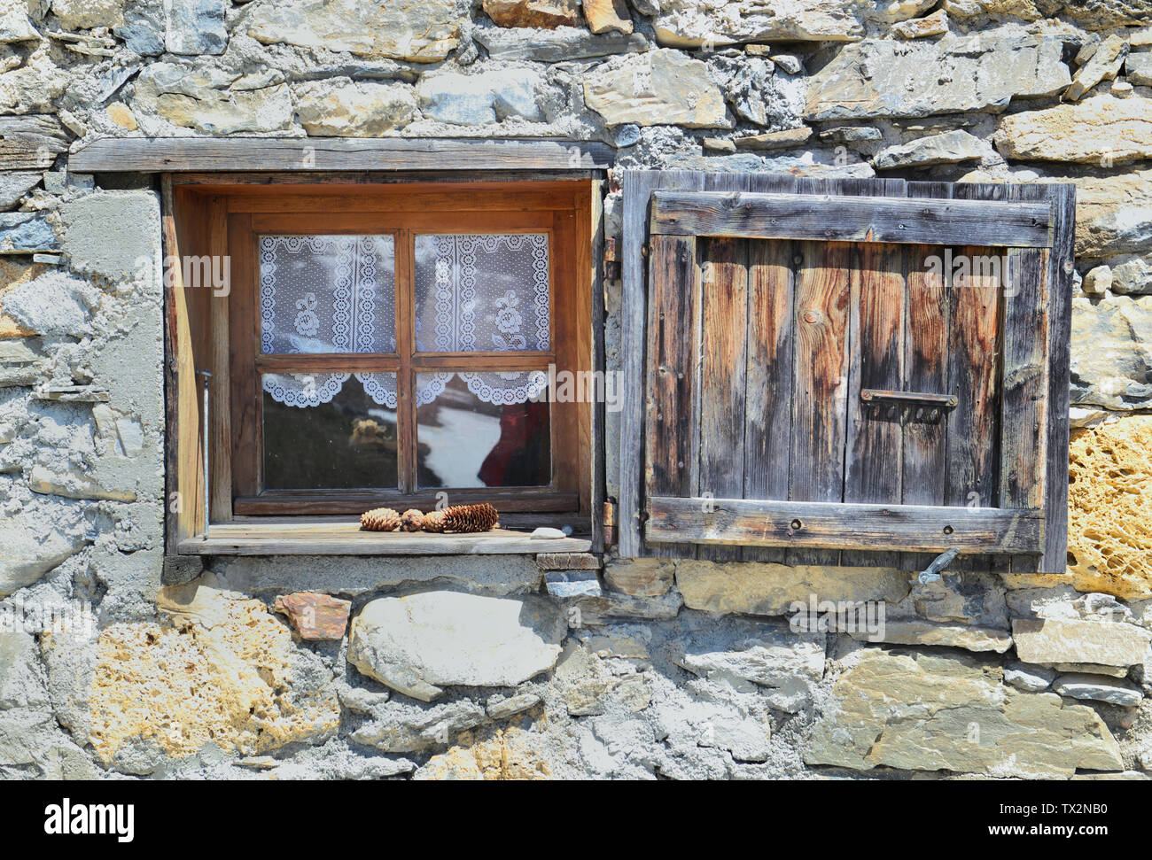 Petite fenêtre et volet sur une façade de pierres d'un vieux chalet de montagne Banque D'Images