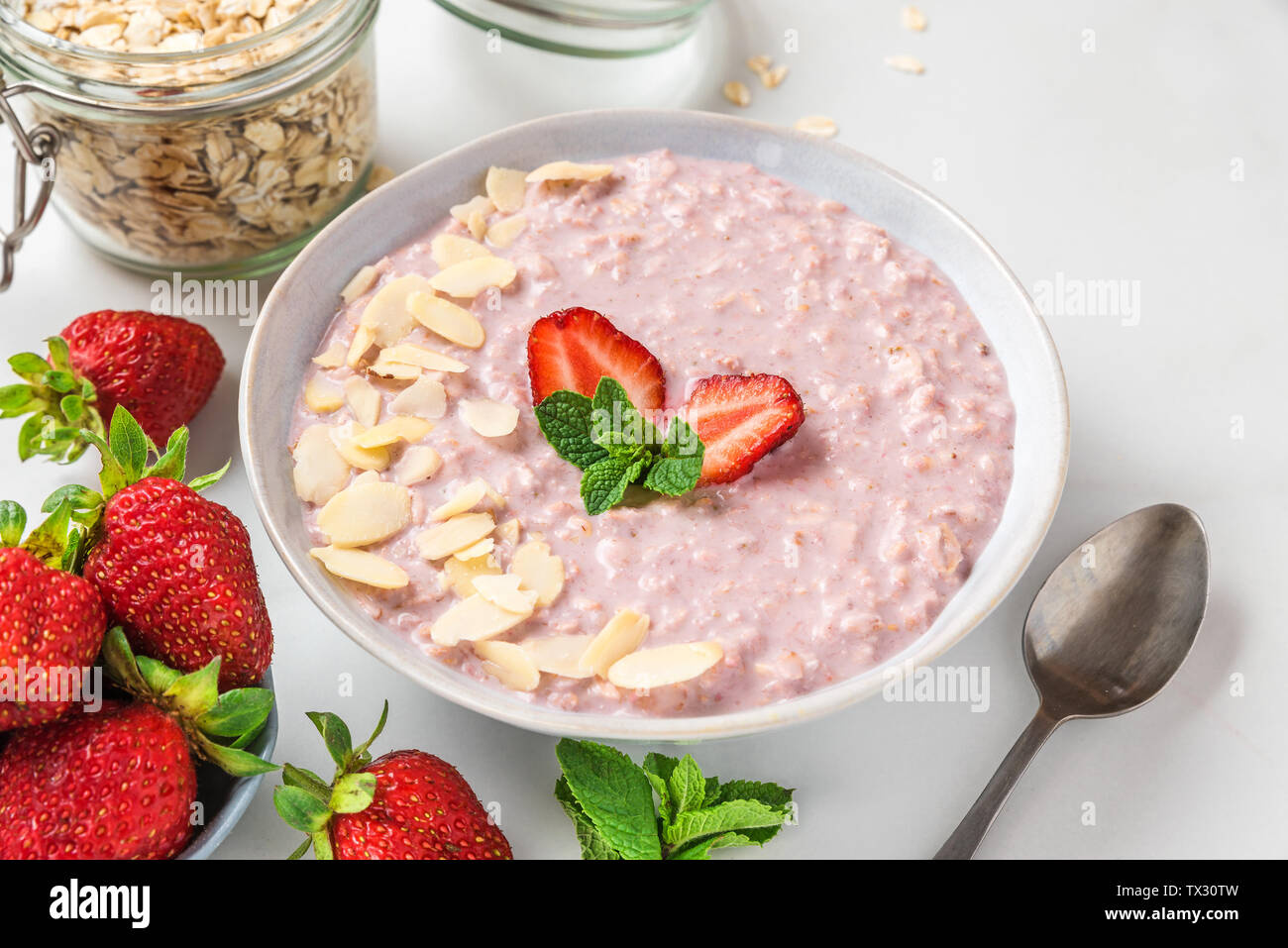 Petit-déjeuner sain. nuit de l'avoine avec des fraises fraîches, amandes et la menthe dans un bol avec une cuillère à table de marbre blanc. close up Banque D'Images