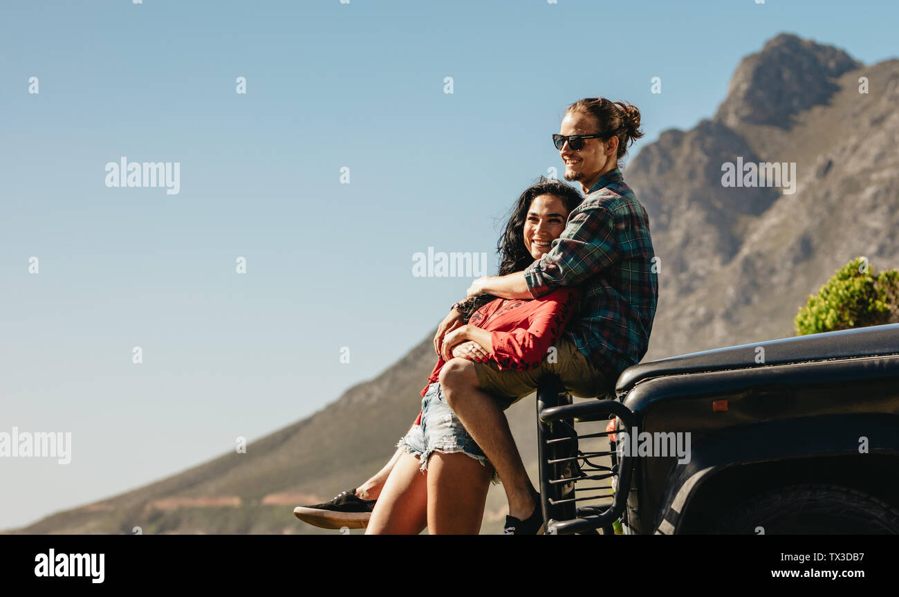 Homme assis sur un capot de voiture et s'étreindre sa petite amie. Couple aimant sur un roadtrip. Banque D'Images