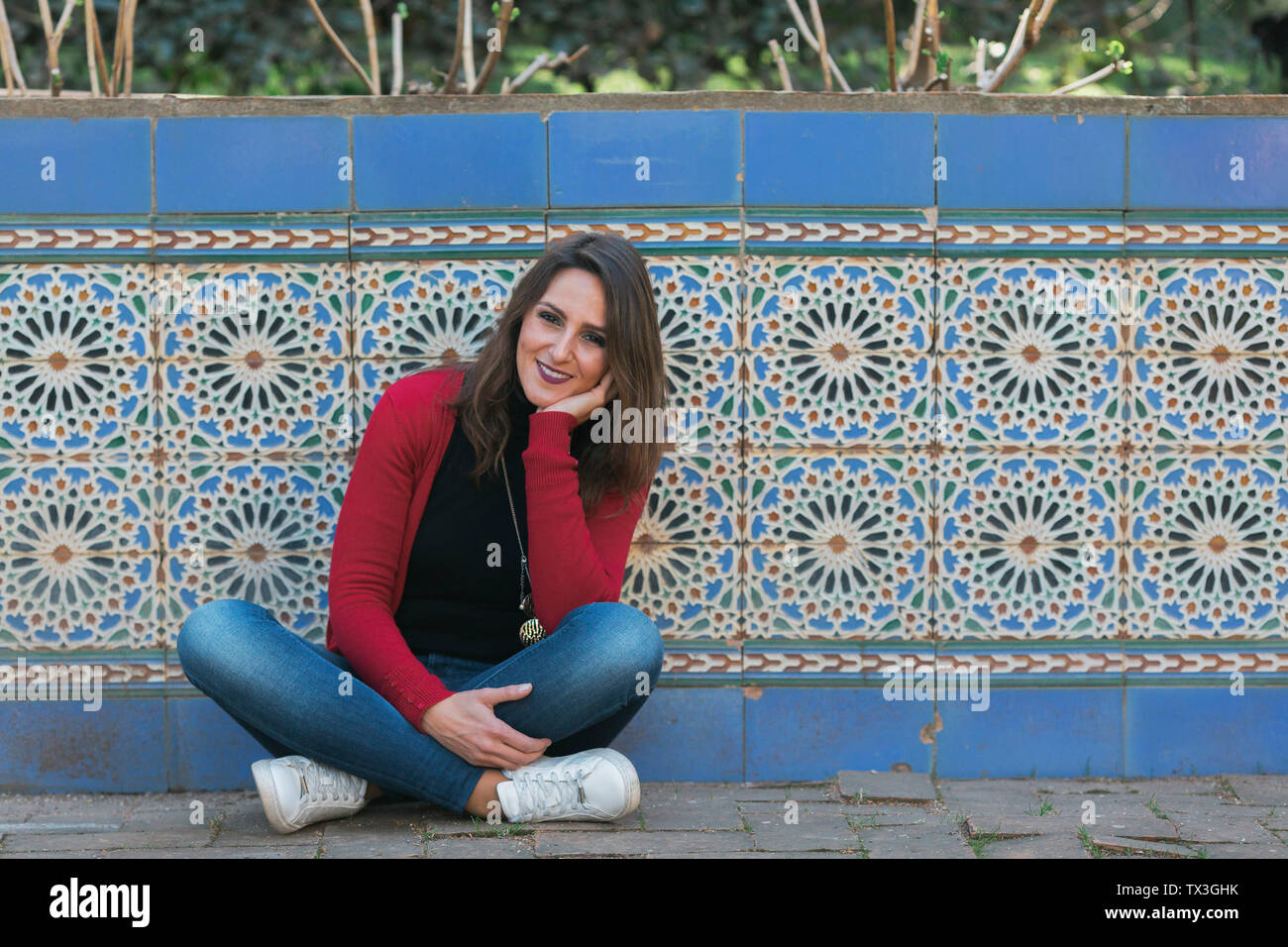 Portrait of smiling woman sitting le long mur de mosaïque Banque D'Images