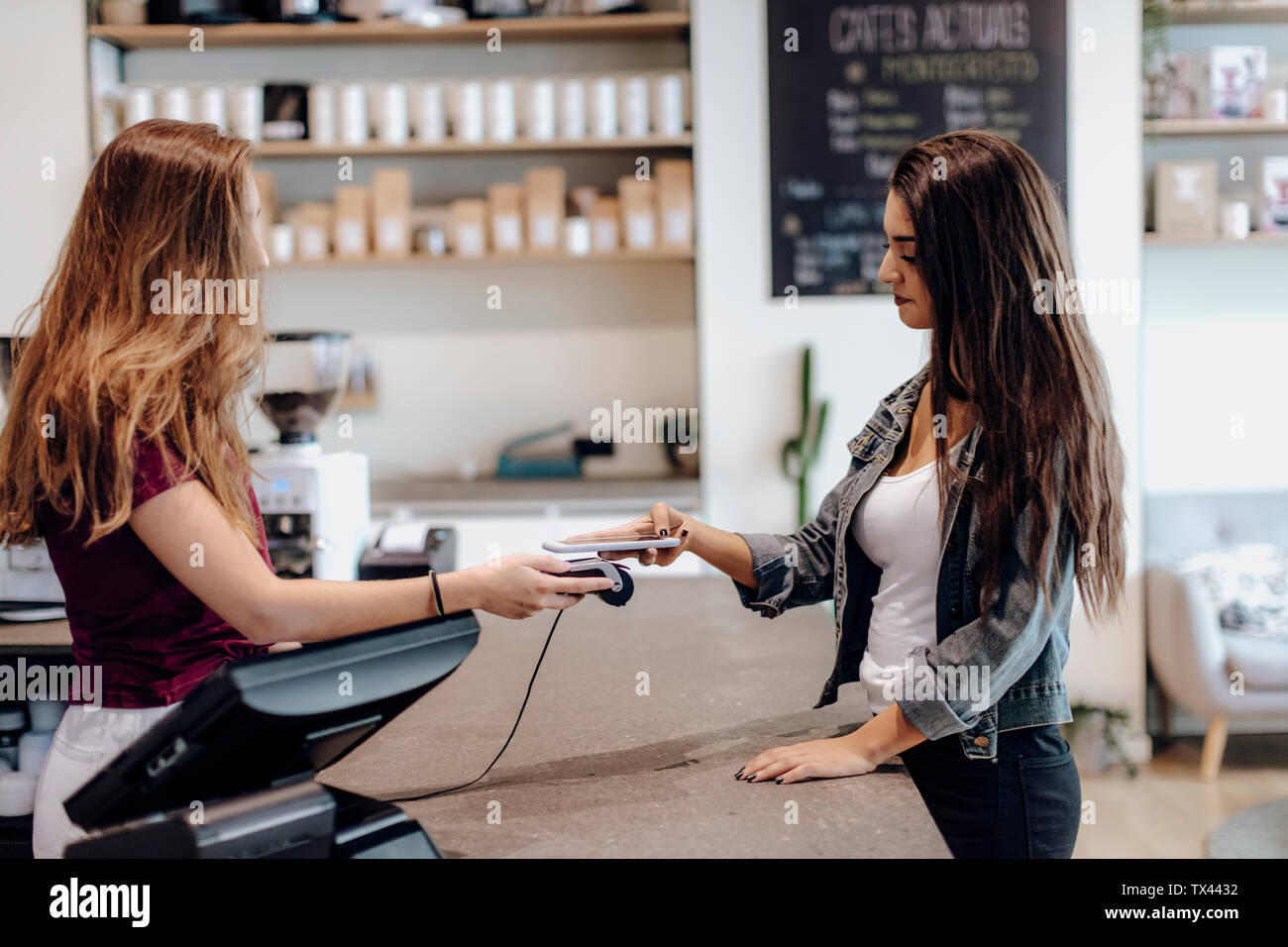 Jeune femme de payer sans espèces avec le smartphone au comptoir d'un café Banque D'Images