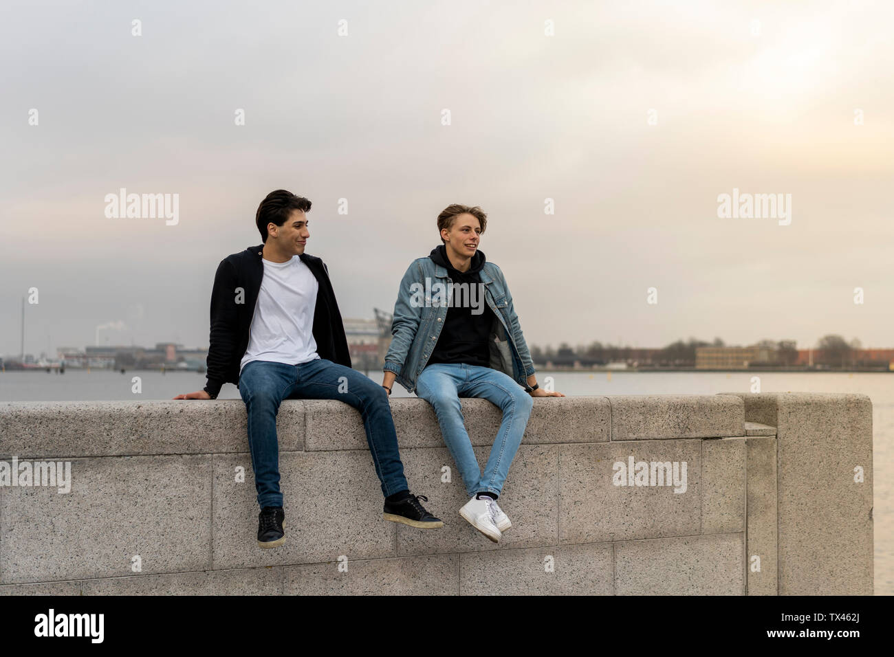 Danemark, Copenhague, deux jeunes hommes assis sur un mur au bord de l'eau Banque D'Images