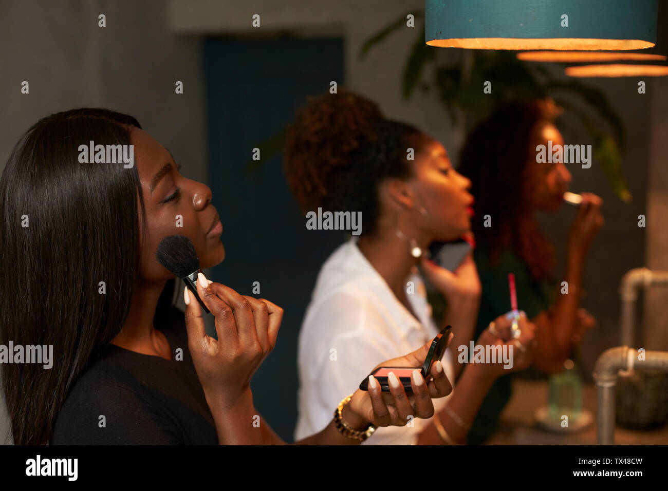 Trois amis appliquant le maquillage au Ladies' room Banque D'Images