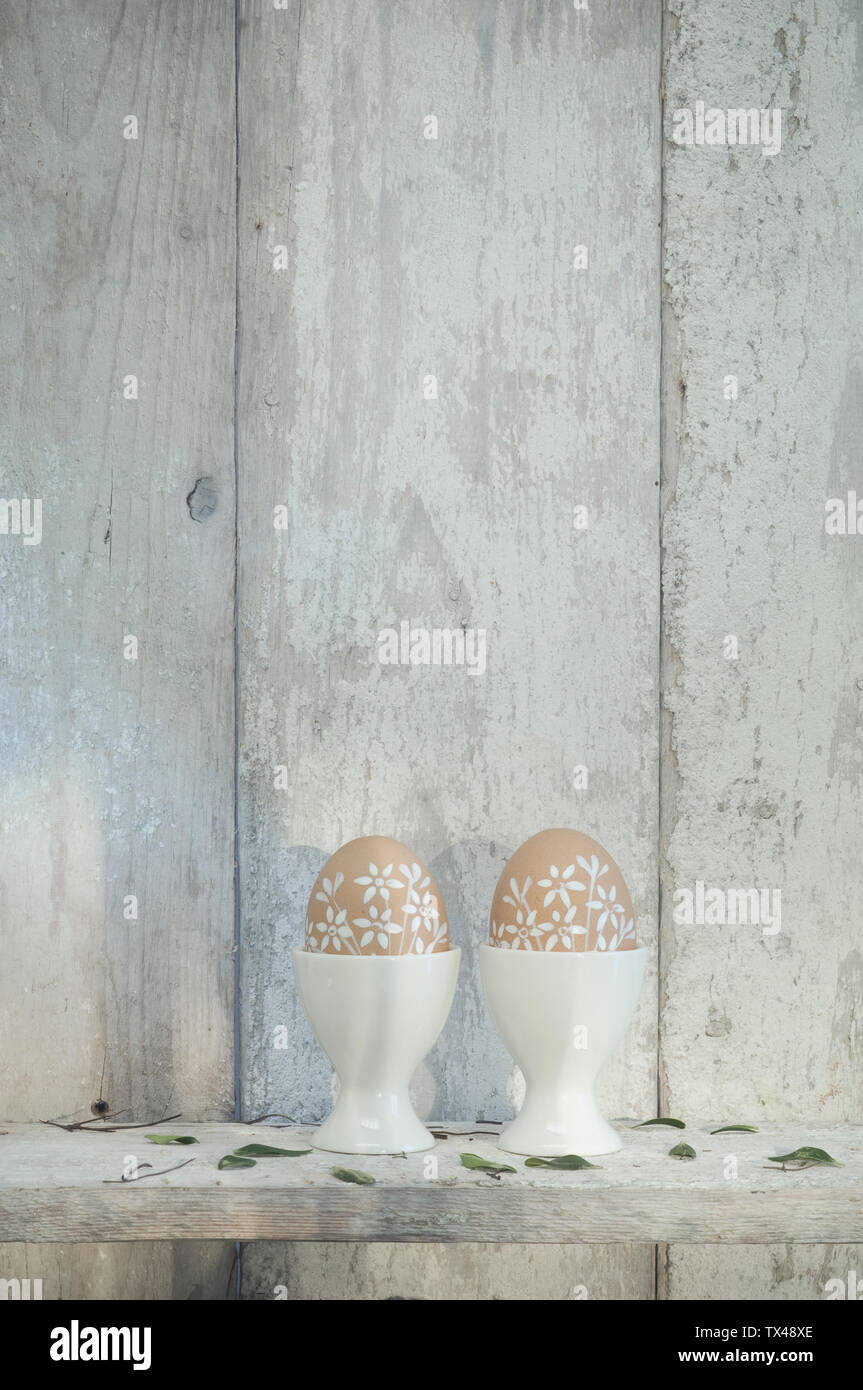 Deux oeufs de Pâques peints dans les tasses sur la tablette en face de mur en bois Banque D'Images