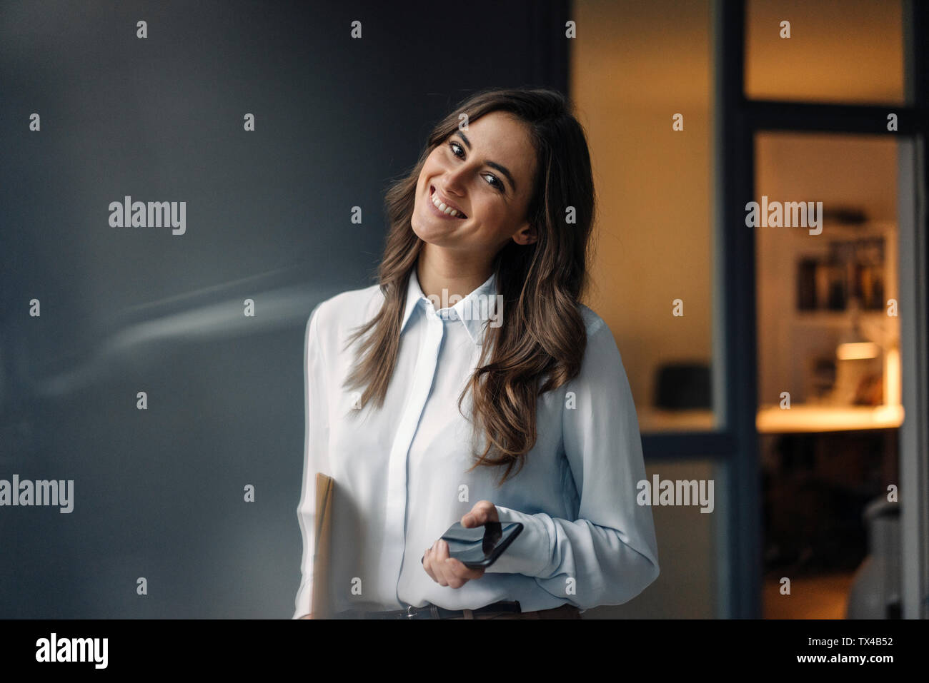 Portrait of smiling young businesswoman holding folder et cell phone Banque D'Images
