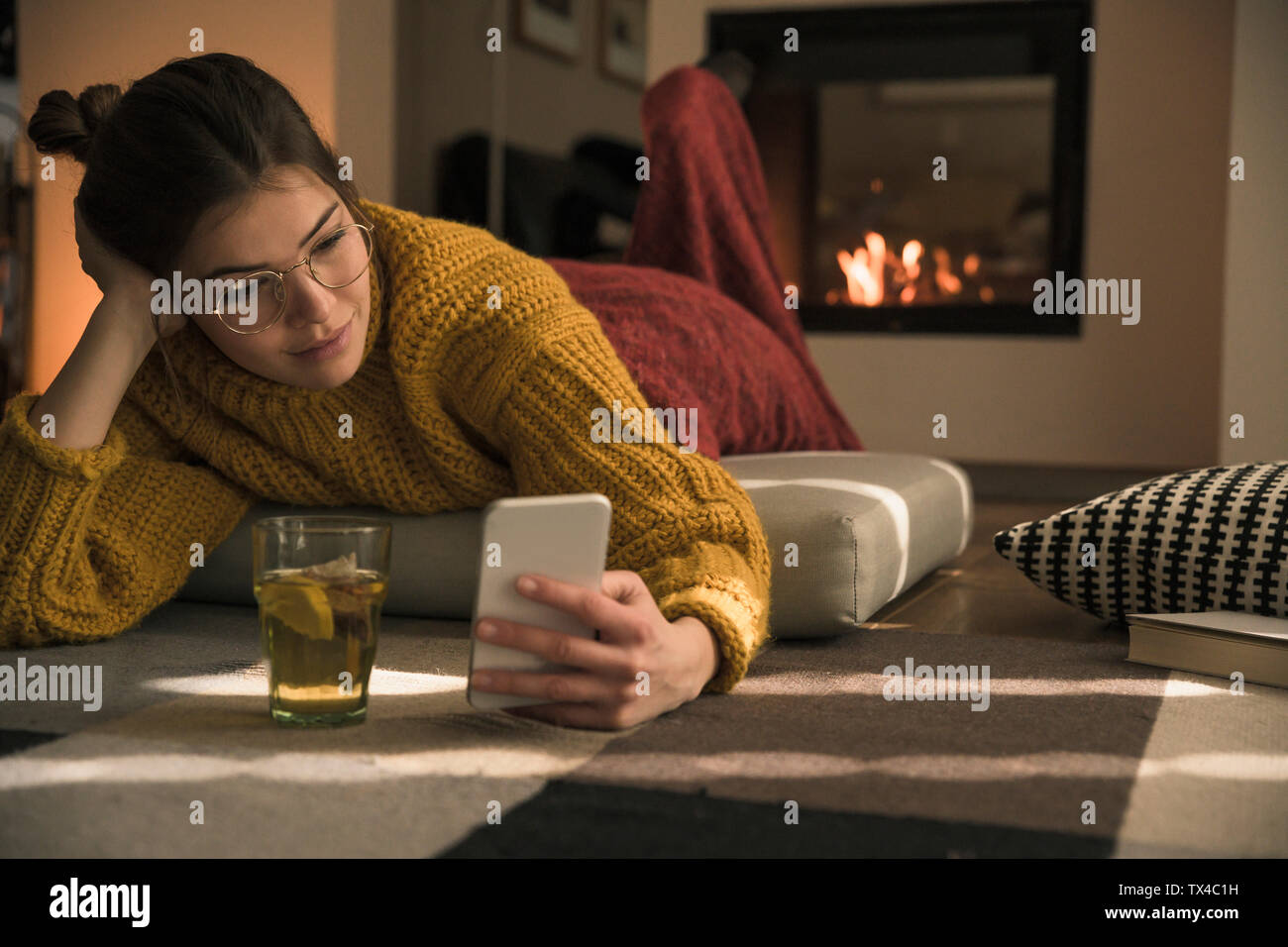 Young woman lying on amortir à la maison using cell phone Banque D'Images