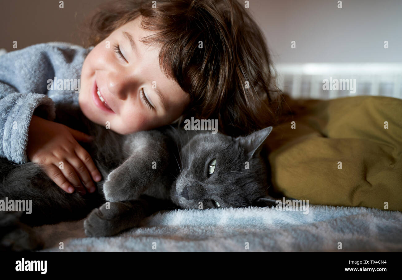 Portrait of happy woman cuddling gray cat lying on bed Banque D'Images