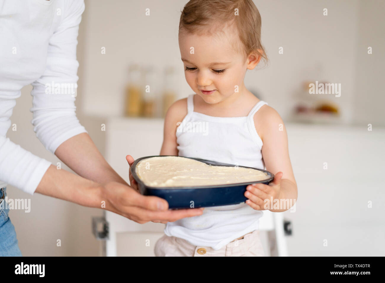 Petite fille et mère tenant un moule avec la pâte à gâteau ensemble dans la cuisine à la maison Banque D'Images