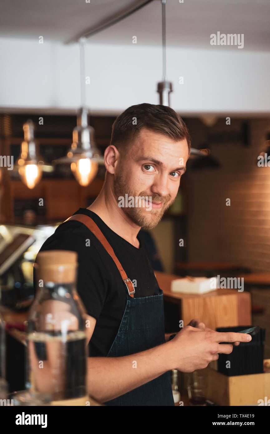 Portrait of smiling barista using mobile phone in coffee shop Banque D'Images
